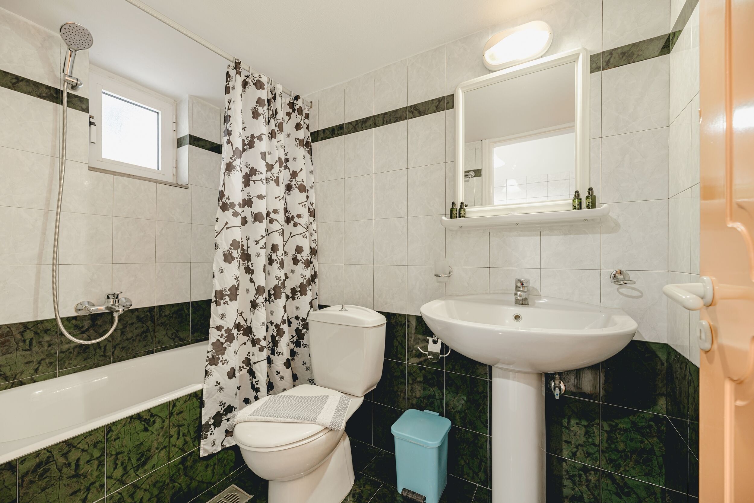 Et badeværelse med toilet, vask, brusebad og et vindue.