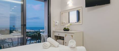A hotel room with a bed, a TV, a bathroom vanity, and a view of the sea.