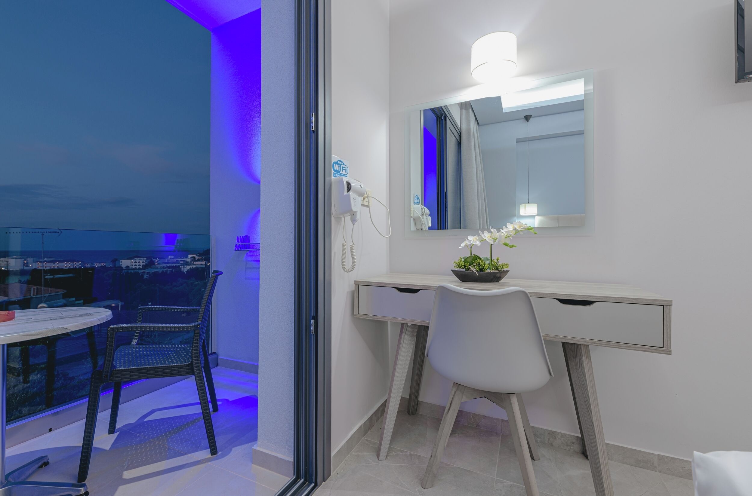 Habitació d'hotel moderna amb un balcó, un escriptori amb una cadira, un mirall i una petita planta en test.