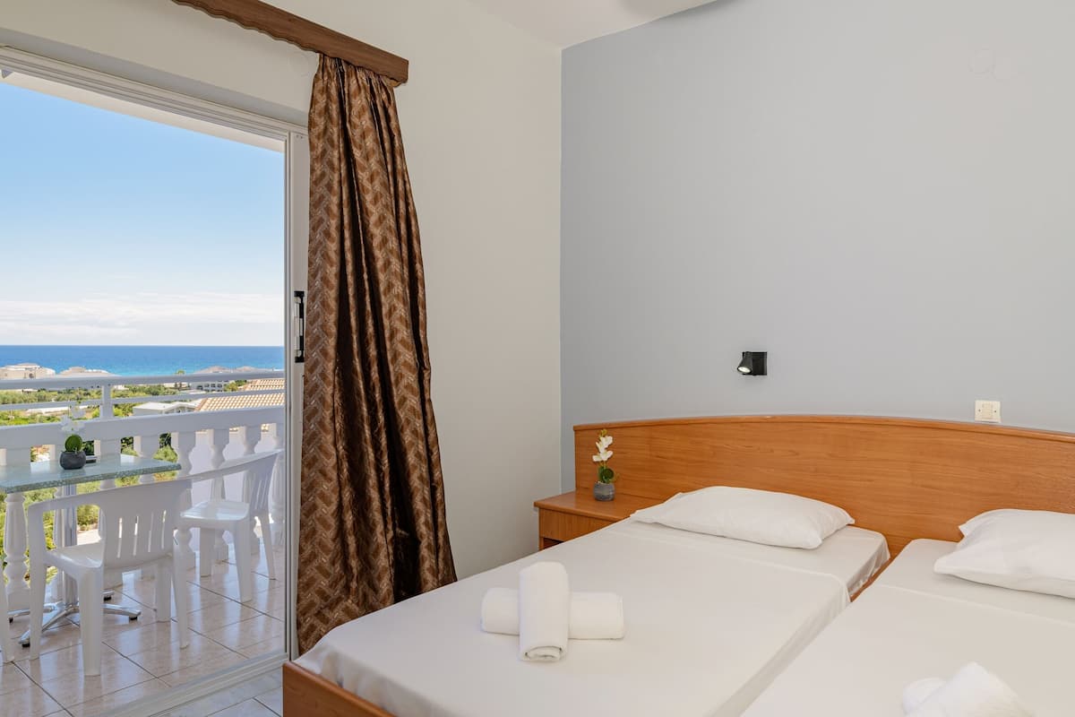 A hotel room with a balcony, a bed with white linens, and a view of the sea.