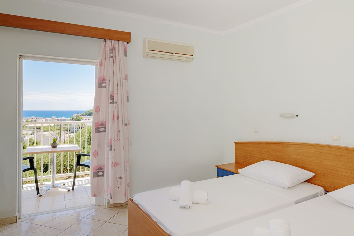 A hotel room with two beds, a balcony with a table and chairs, and a view of the city.