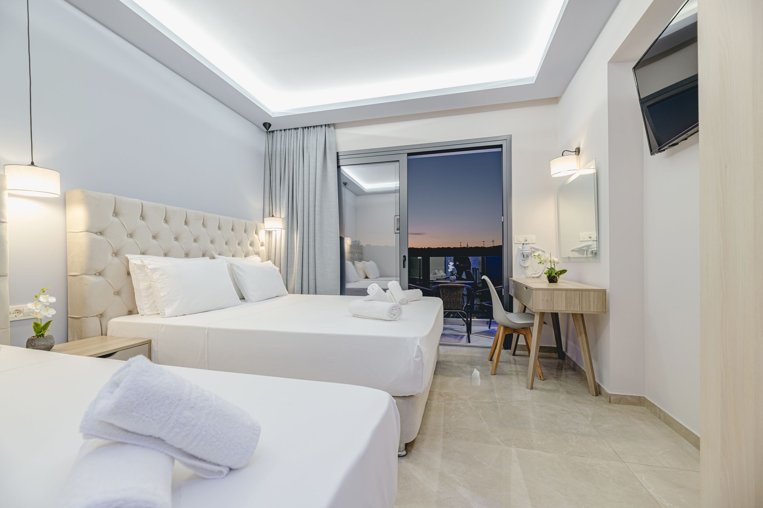Habitació d'hotel moderna amb dos llits, un escriptori i un gran finestral amb vista al capvespre.
