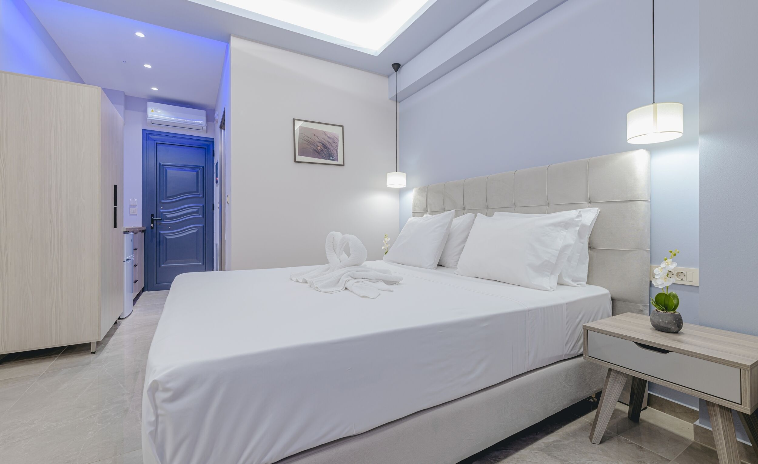 Una habitación de hotel moderna con una cama grande, una mesita de noche, un armario y una lámpara en el techo.