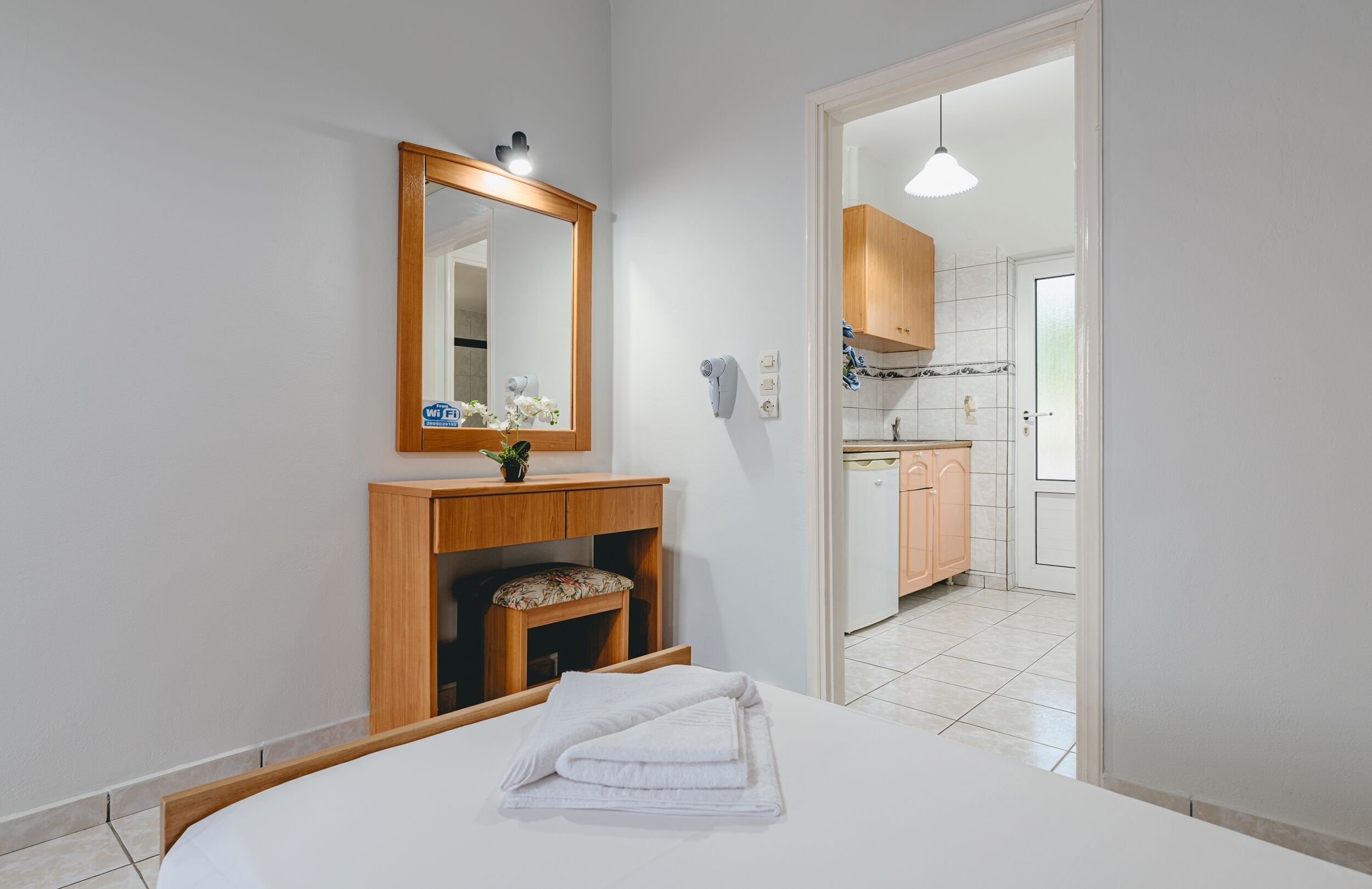 Un dormitorio con una cama, una mesita de noche de madera, un espejo y vistas hacia una zona de cocina.
