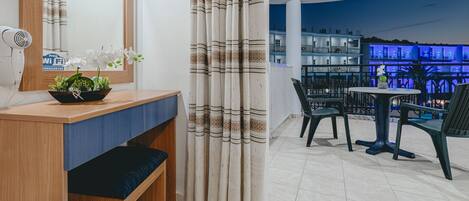 A modern hotel room with a wooden desk, a bench, a mirror, and a view of the pool area at night.