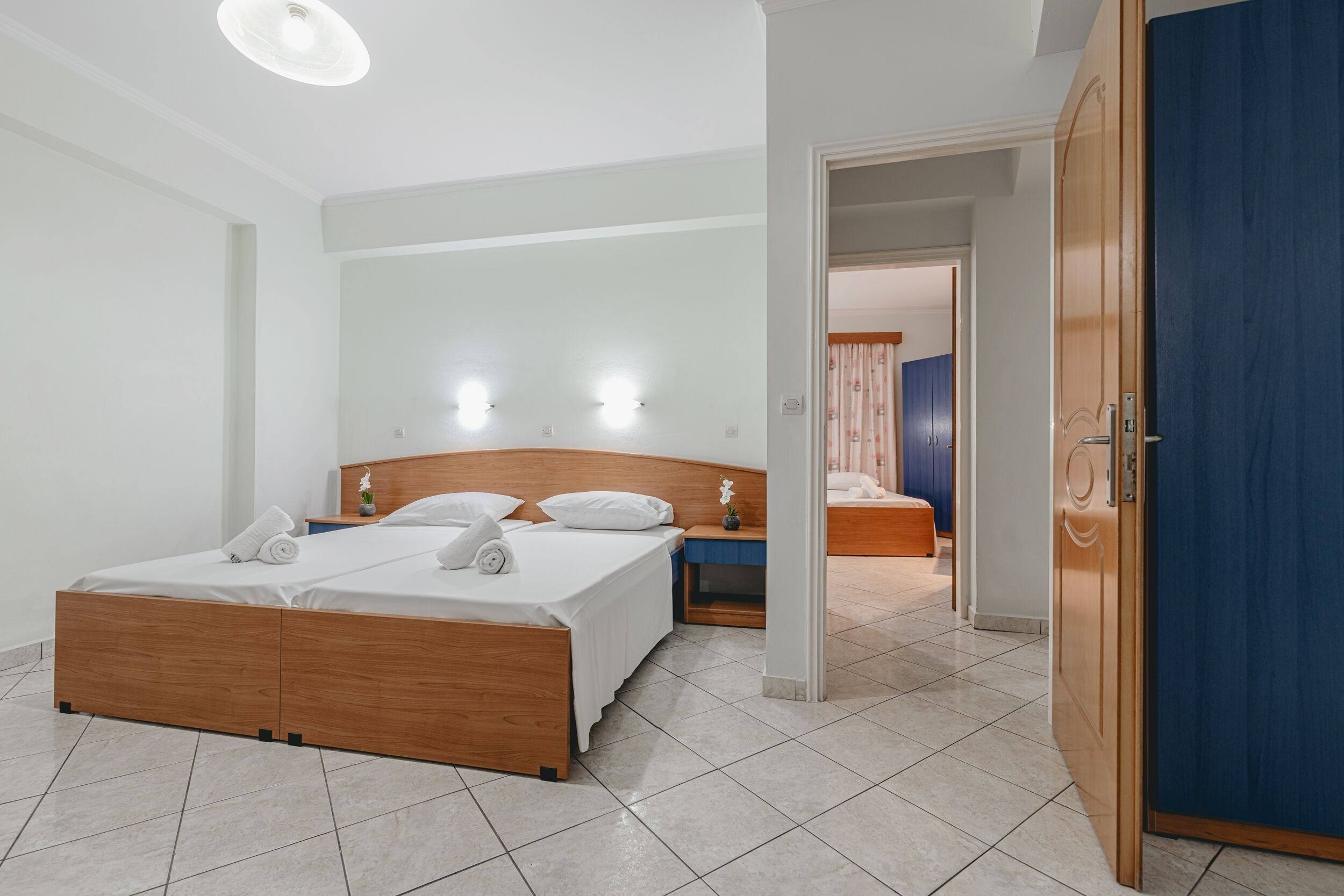 A modern hotel room with a wooden bed, a nightstand, and a blue door.