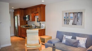 Un espacio habitable compacto con kitchenette, zona de estar con sofá y sillones, y ventana con vista a un edificio.