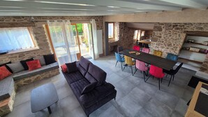 A spacious living area with a dark sofa, a dining table with colorful chairs, and stone walls. - LE COTTAGE DE JOUSSEAUME (Mortagne-sur-Sèvre)