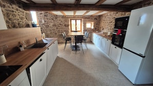 A kitchen with stone walls, wooden beams, a white refrigerator, and a dining table with chairs. - LE COTTAGE DE JOUSSEAUME (Mortagne-sur-Sèvre)