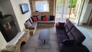 A cozy living area with a stone fireplace, a sofa, and a TV mounted on the wall. - LE COTTAGE DE JOUSSEAUME (Mortagne-sur-Sèvre)