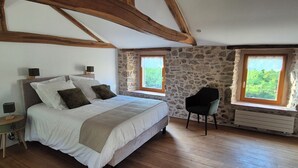 A bedroom with a bed, two bedside tables, a chair, and two windows with views of greenery. - LE COTTAGE DE JOUSSEAUME (Mortagne-sur-Sèvre)