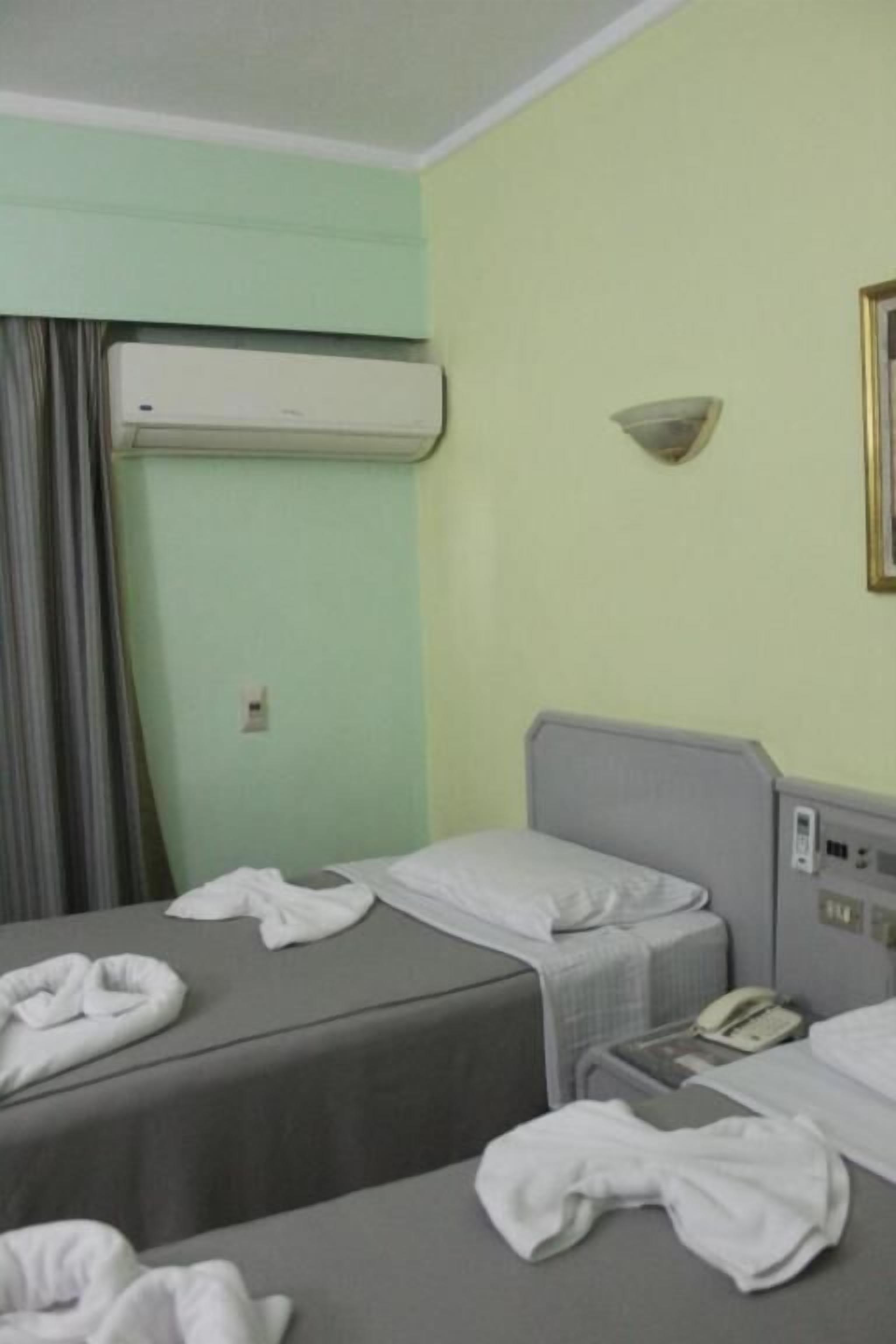 A hotel room with two beds, an air conditioning unit, a bedside telephone, and a wall-mounted light fixture.