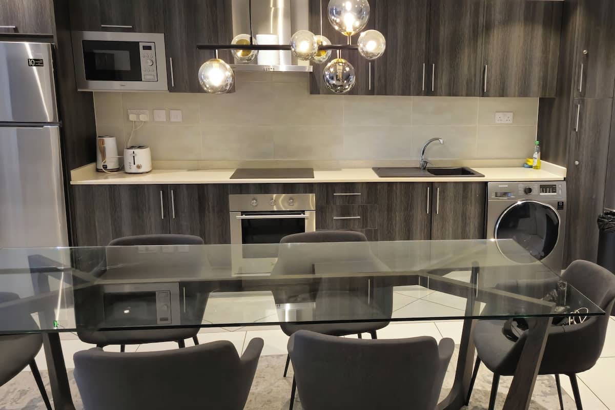 Une cuisine moderne avec une table à manger en verre, des meubles de rangement en bois foncé, des appareils électroménagers en acier inoxydable et un four encastré.
