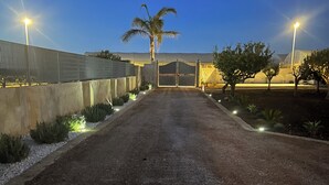 A gravel driveway leading to a gated entrance with a palm tree and small shrubs on either side. - Nausicaa Guesthouse in Marsala Igloo in an oasis among the sea, olive trees and vineyards - 1 (Sicilia)