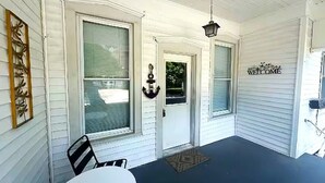 A covered porch with a white door, a welcome sign, a hanging lantern, and a table with chairs. - The Perfect Getaway 2-bedroom apartment in wonderful Sandusky with WiFi, AC (Sandusky)