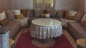 Una sala de estar con una mesa redonda, sofás, cojines estampados, una araña y un equipo de aire acondicionado.