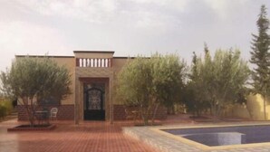 A building with a central entrance, a brick pathway leading to it, and a pool area to the right. - At Sondos (Marrakech)