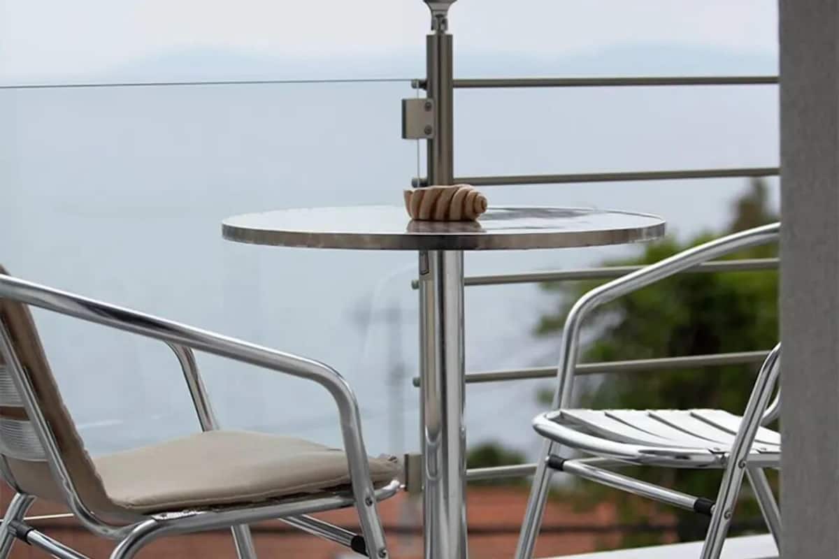 A balcony with two metal chairs and a small round table, overlooking a body of water.
