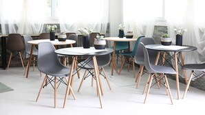 A modern dining area with round tables and chairs, white curtains, and potted plants. - Agapaki Studios (Neos Marmaras)