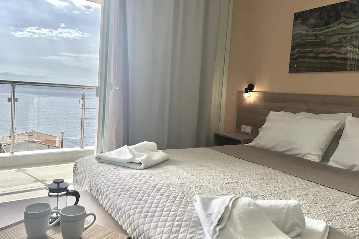 A hotel room with a large bed, a nightstand, a coffee maker, and a view of the sea.