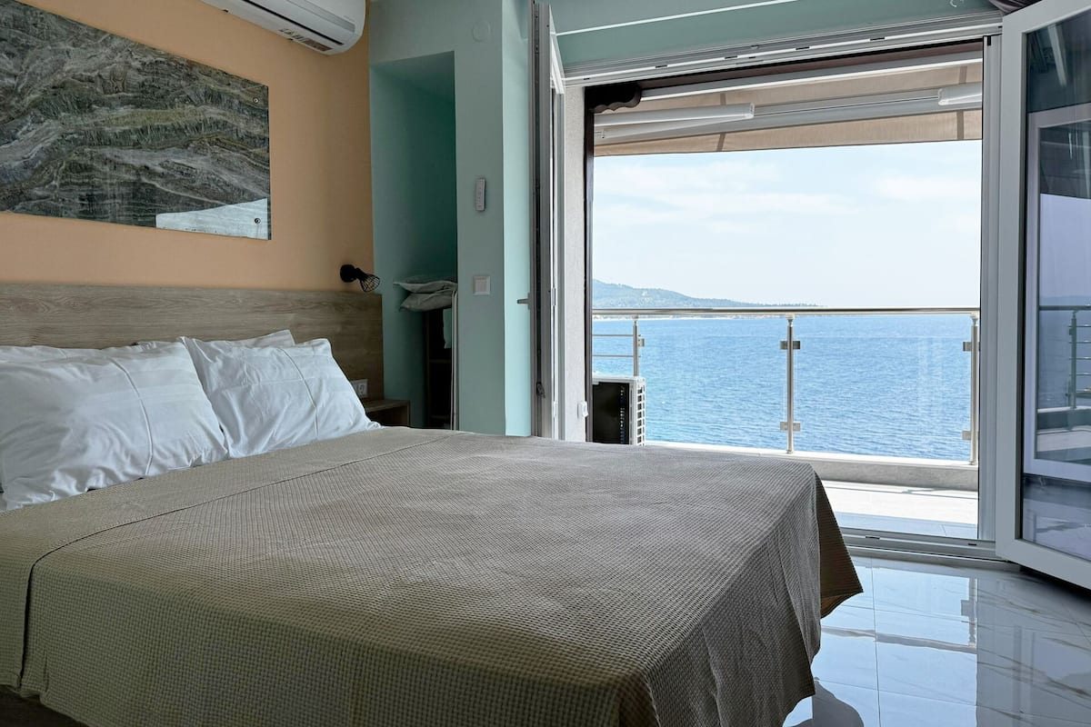 A bedroom with a large bed, a view of the sea, and a sliding glass door leading to a balcony.