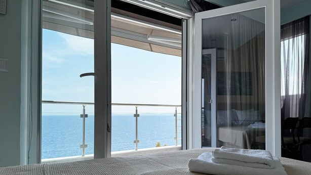 A room with a large sliding glass door leading to a balcony with a view of the sea. - Agapaki Studios (Neos Marmaras)