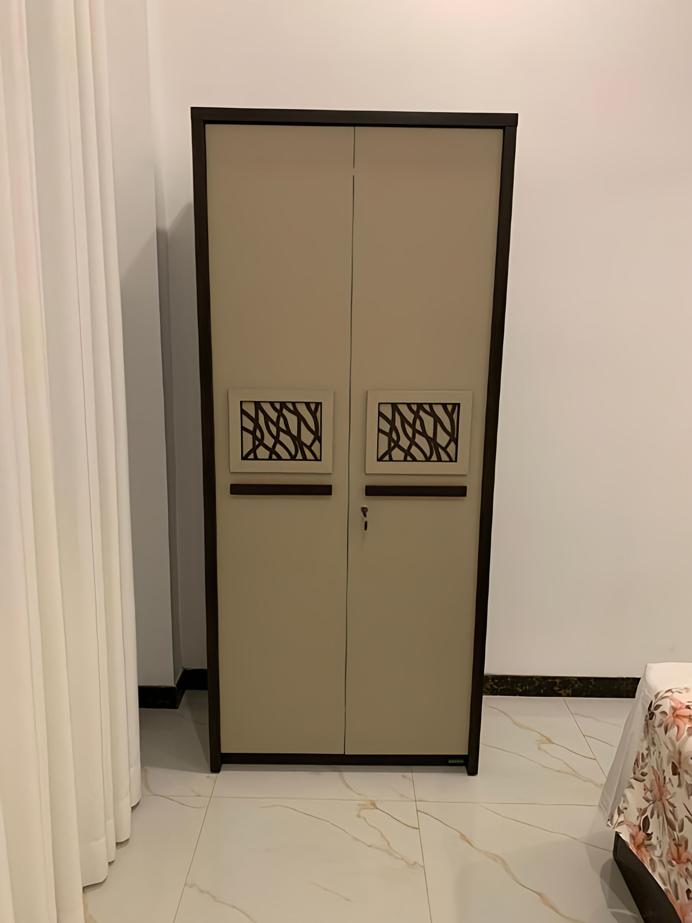 A wardrobe with two doors, each with a decorative panel, in a room with a bed and curtains.