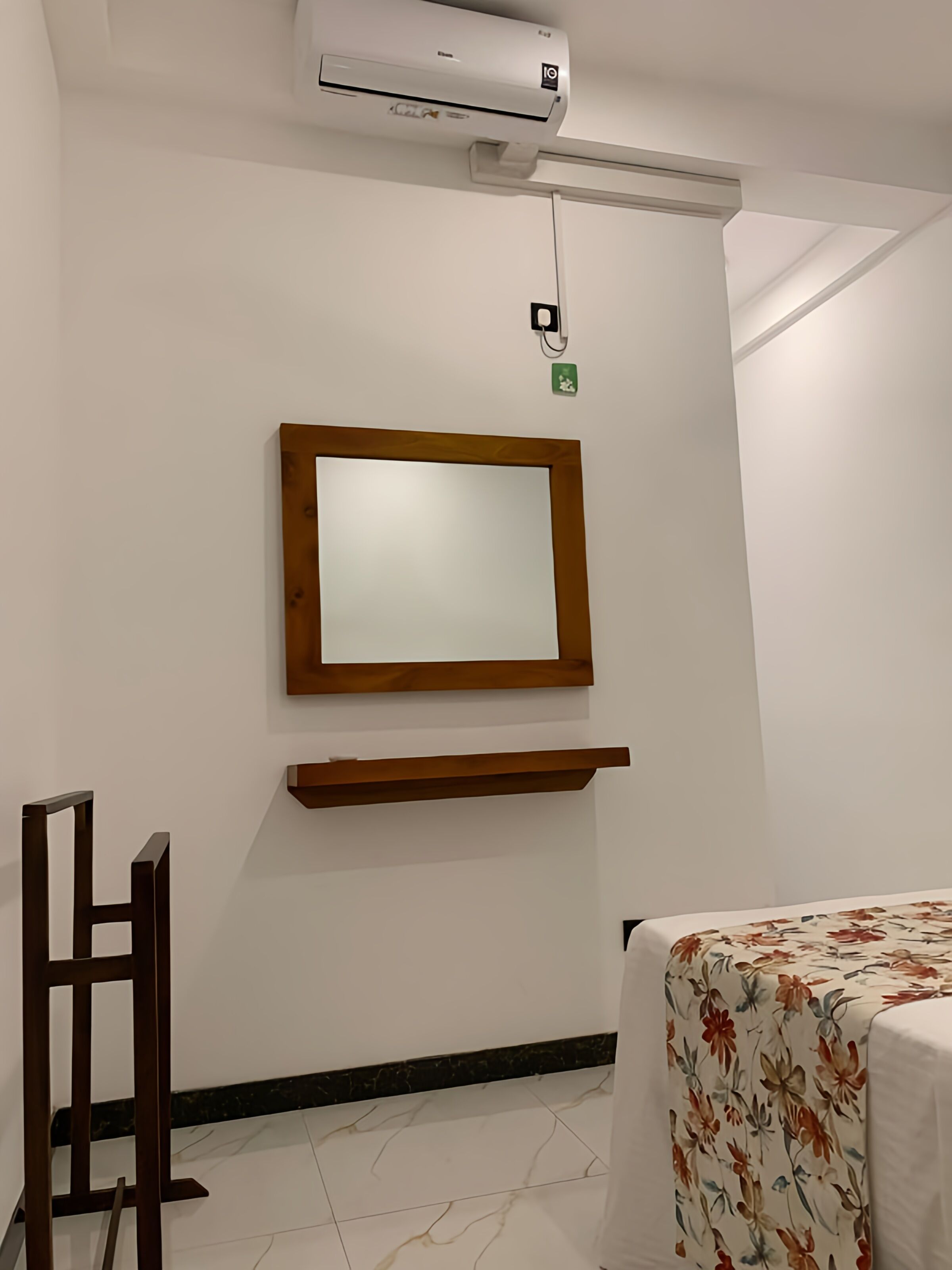 A room with a bed, a wooden chair, a wall-mounted TV, and a small shelf.