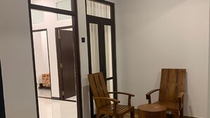 Una habitación con dos sillas de madera y una mesa redonda, una puerta con un espejo, y una alfombra estampada en el suelo.