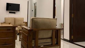 Una sala moderna con ventilador de techo, televisor de pantalla plana, sofá, una silla de madera y un mueble de madera.