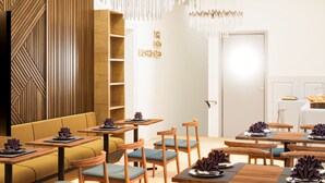 Un espace de restauration moderne, avec des meubles en bois, des luminaires suspendus et un mur orné d’un motif géométrique.