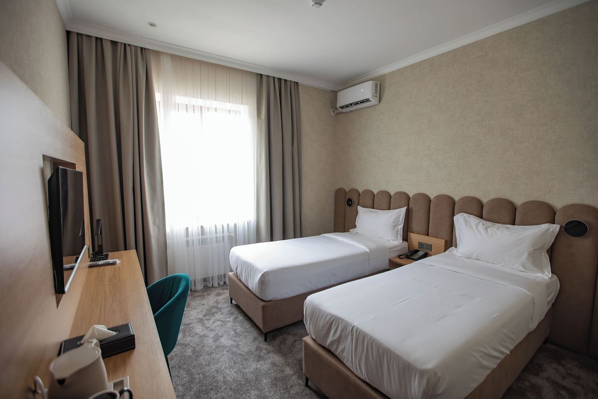 Habitación de hotel con dos camas, un escritorio, una silla y un televisor.