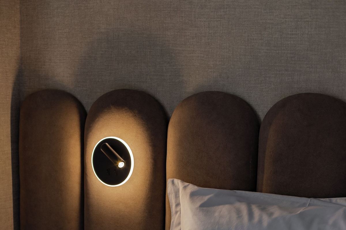Una cama con cabecera que incluye una lámpara circular.