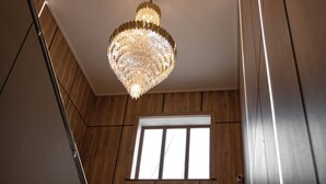Un escalier orné d’un lustre, des murs lambrissés et une fenêtre avec des stores.