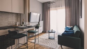Uma sala de estar moderna com sofá, TV e área de cozinha com um banquinho.