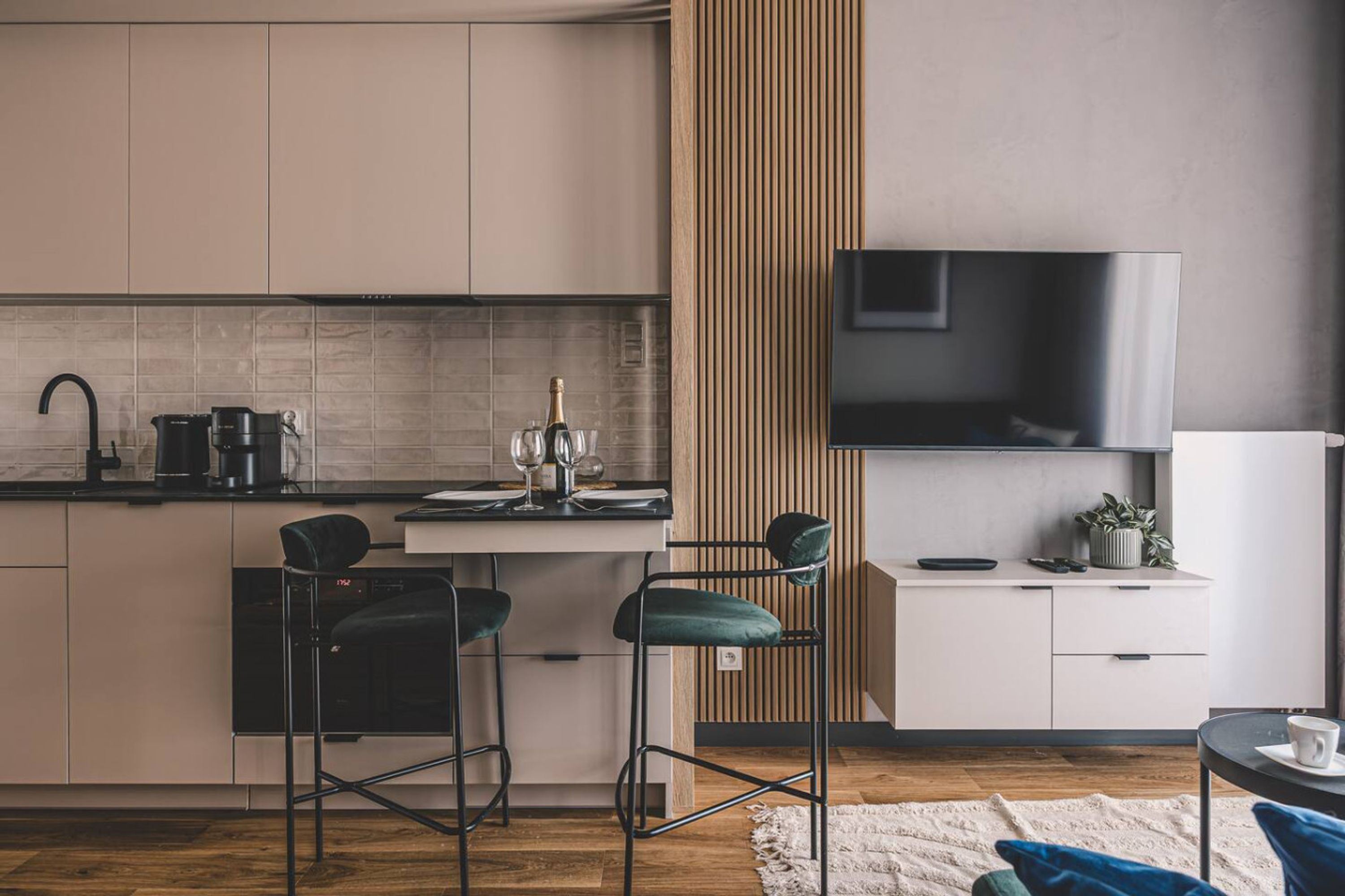 A modern kitchen with a built-in stove, bar stools, and a flat-screen TV mounted on the wall.