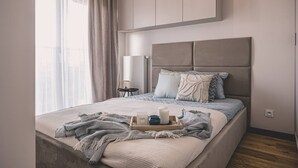 Quarto moderno com cama grande, mesa de cabeceira e janela com cortinas.