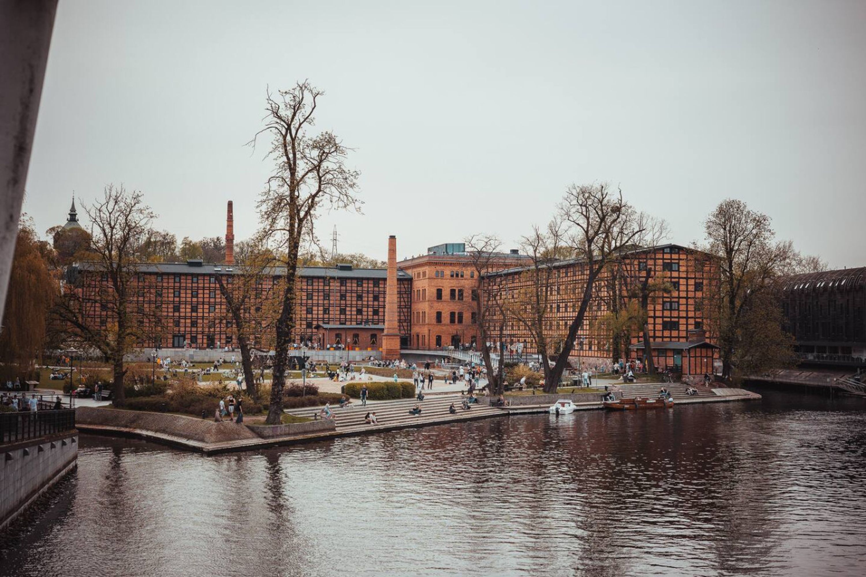 A riverside view with a large brick building, a bridge, and trees.