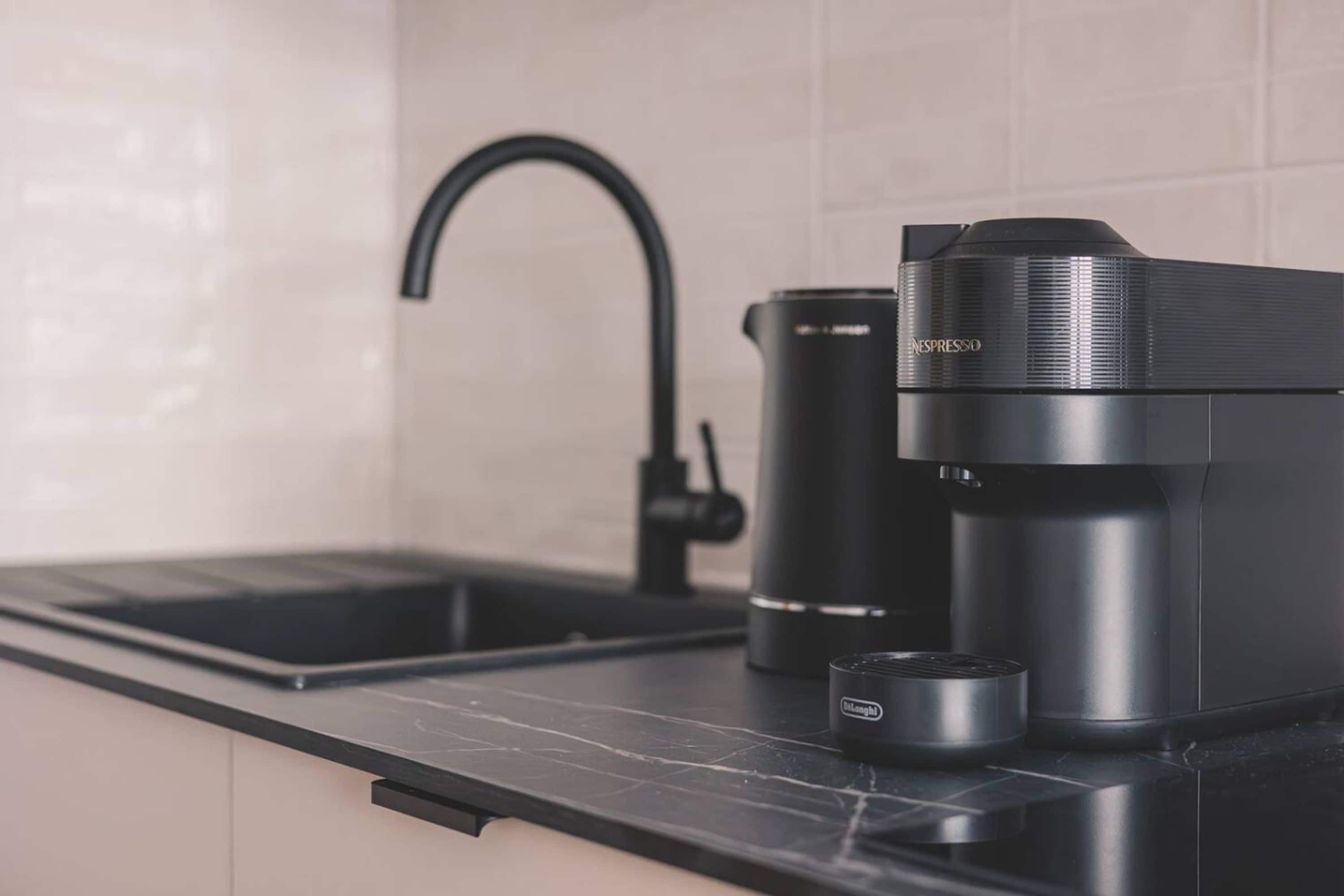 A modern kitchen with a black countertop, a black coffee maker, and a black kettle.