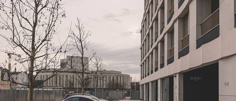 A modern building with a white facade, a parking area with a white car, and a tree in the foreground.