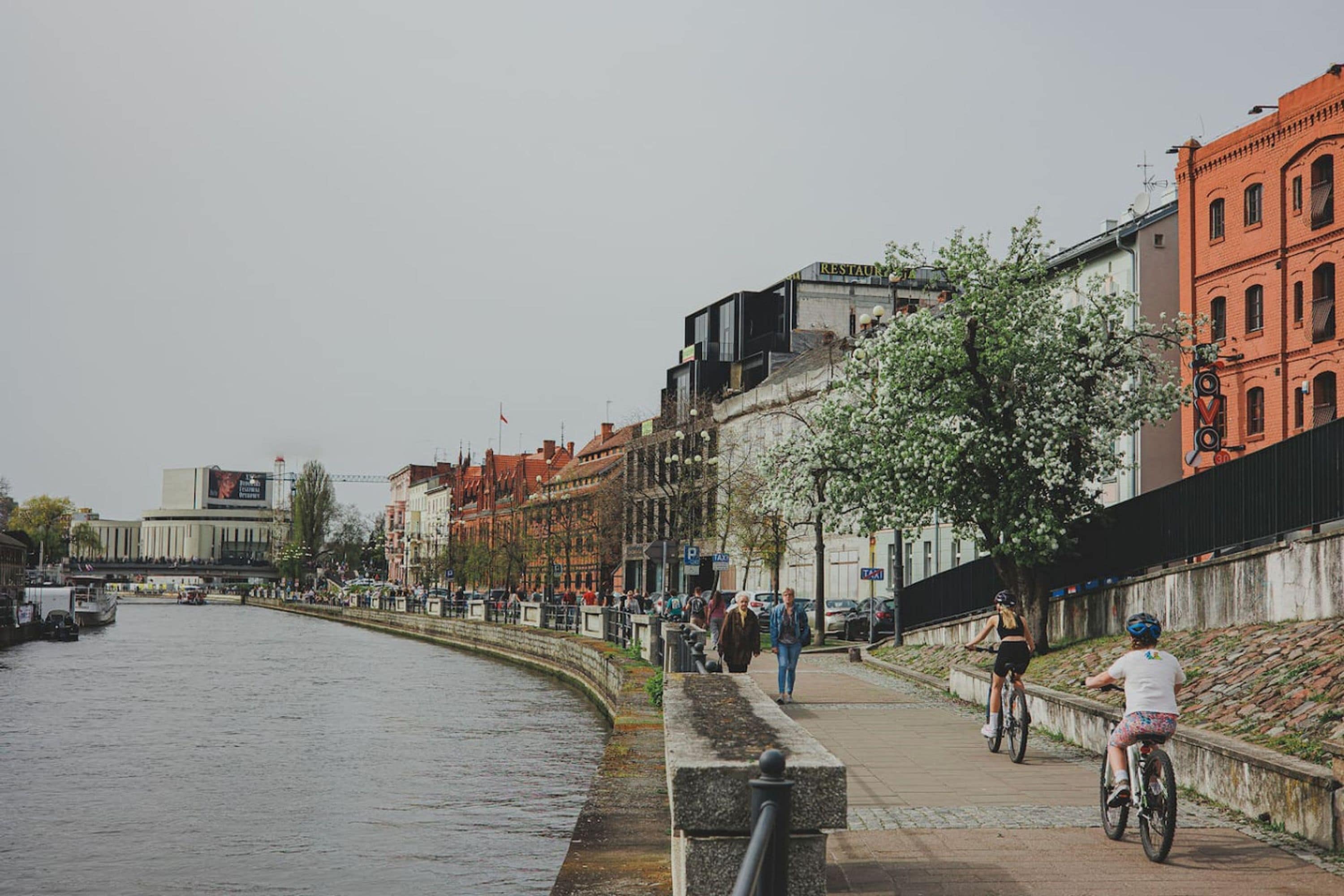 A riverside walkway with buildings, a bike lane, and a pedestrian path.