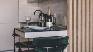 Uma mesa de jantar com duas taças de vinho e uma garrafa de vinho Jaume Serra, numa cozinha moderna com bancada preta e uma cadeira verde.