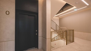 Um elevador moderno com porta escura, escada com corrimão de metal e teto iluminado.