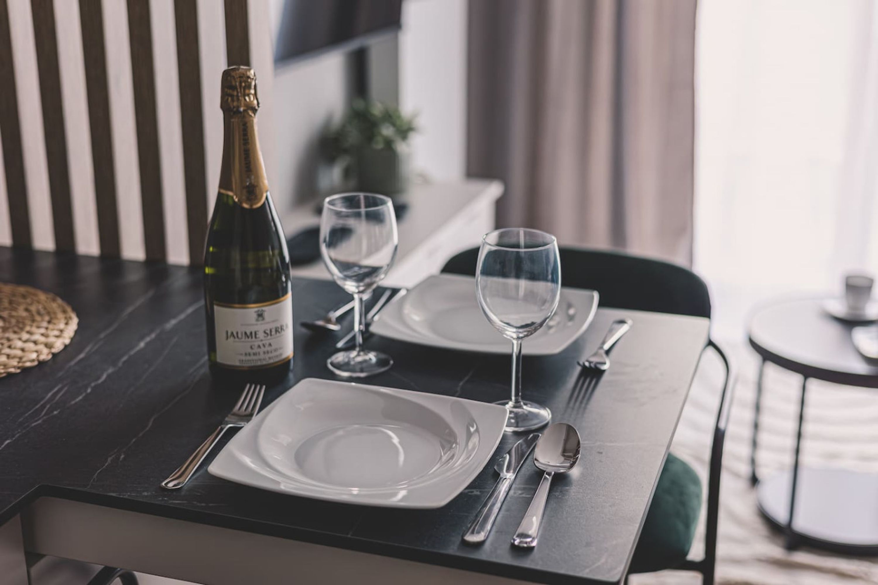 A dining table set with a bottle of Jaume Serra cava, two wine glasses, and cutlery.