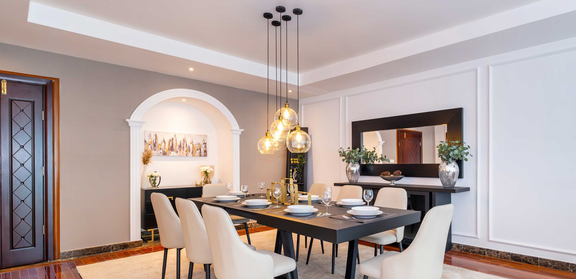 A modern dining room with a long table set for six, elegant chairs, a chandelier, and a cityscape painting on the wall.