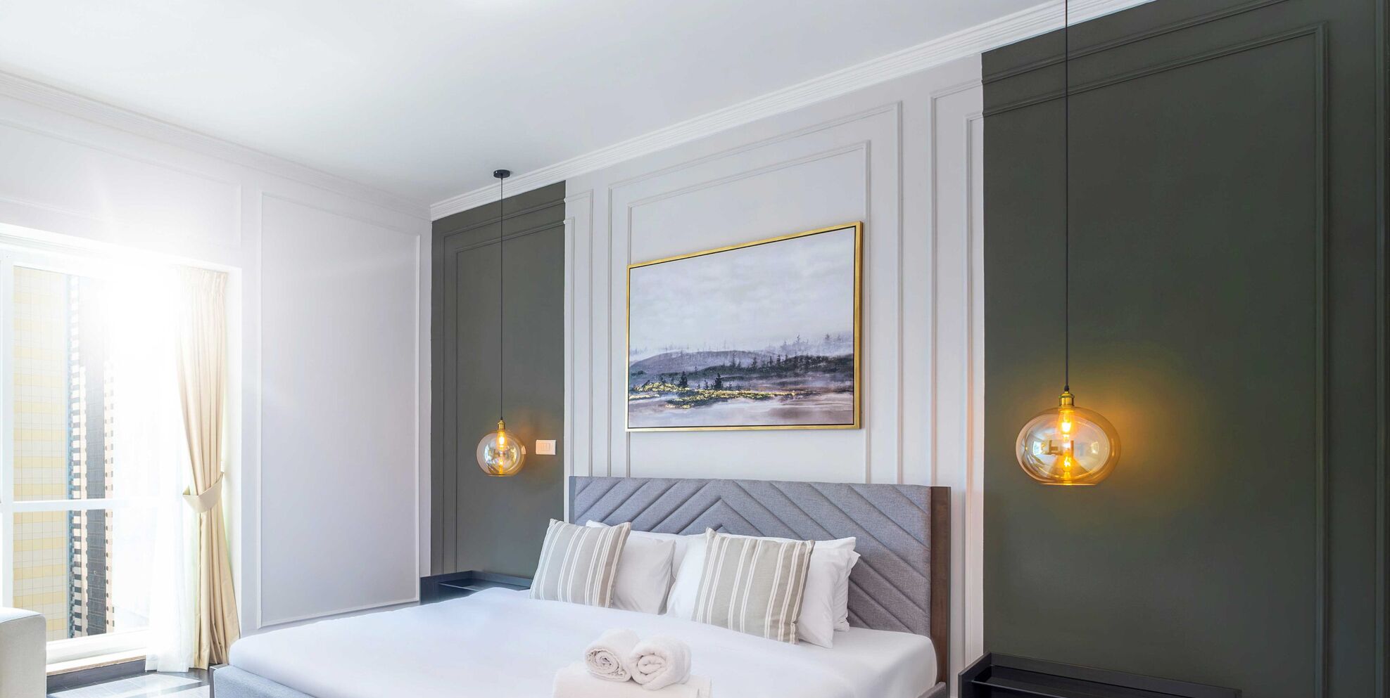 Ett modernt hotellrum med en stor säng, utsikt över stadsbilden och två hänglampor.