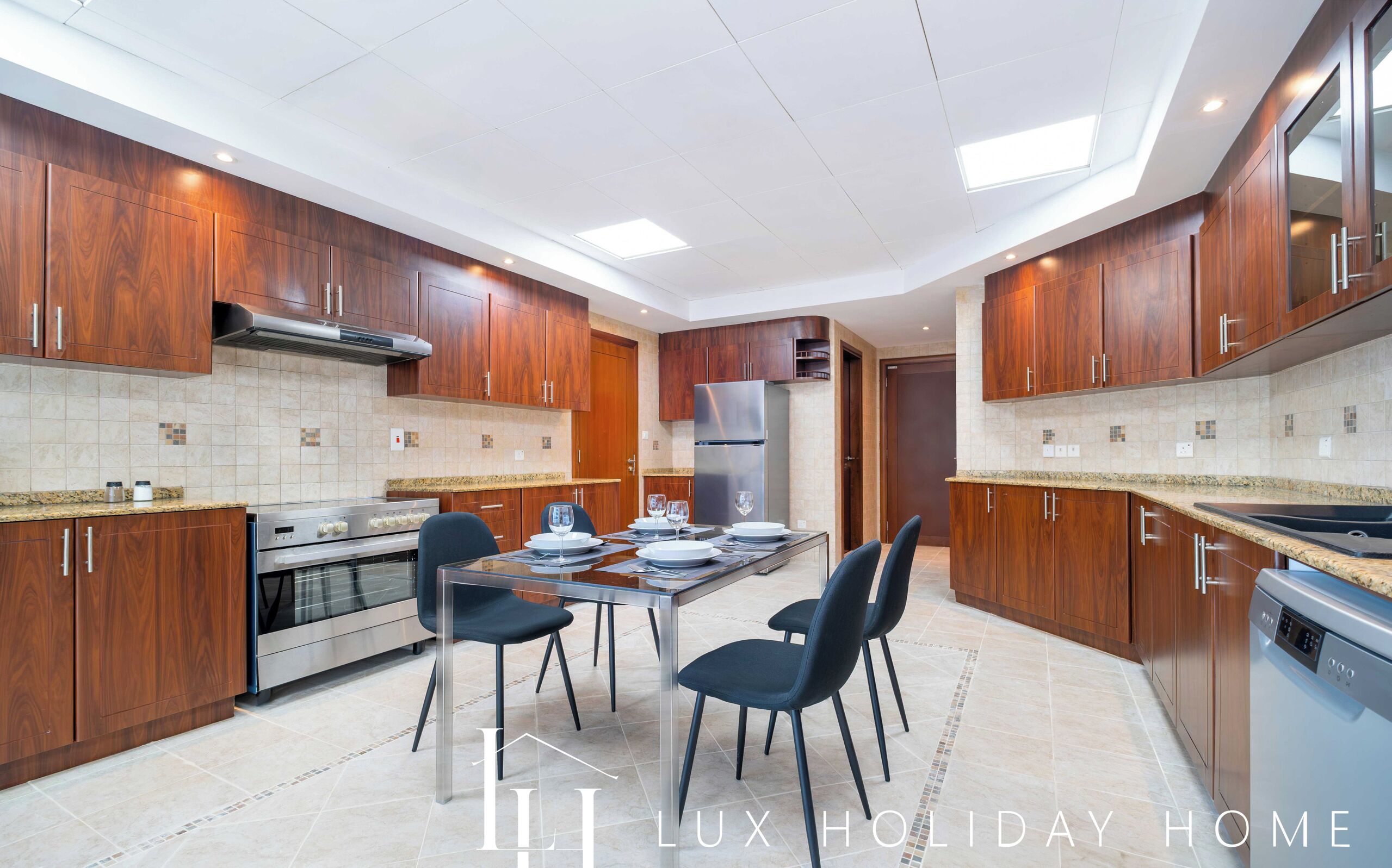 A modern kitchen with wooden cabinets, stainless steel appliances, and a dining area with two chairs and a table set for two.