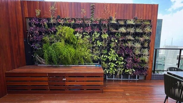 Eine Holzterrasse mit einer Bank und einer vertikalen Gartenwand.