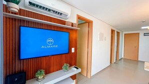 Ein Empfangsbereich mit einem Flachbildfernseher, der das ALMARE-Logo zeigt, Holzvertäfelung, einer kleinen Pflanze und einem Empfängerservice-Schalter.
