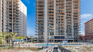 A multi-story hotel with balconies, a pool area, and a beach view.